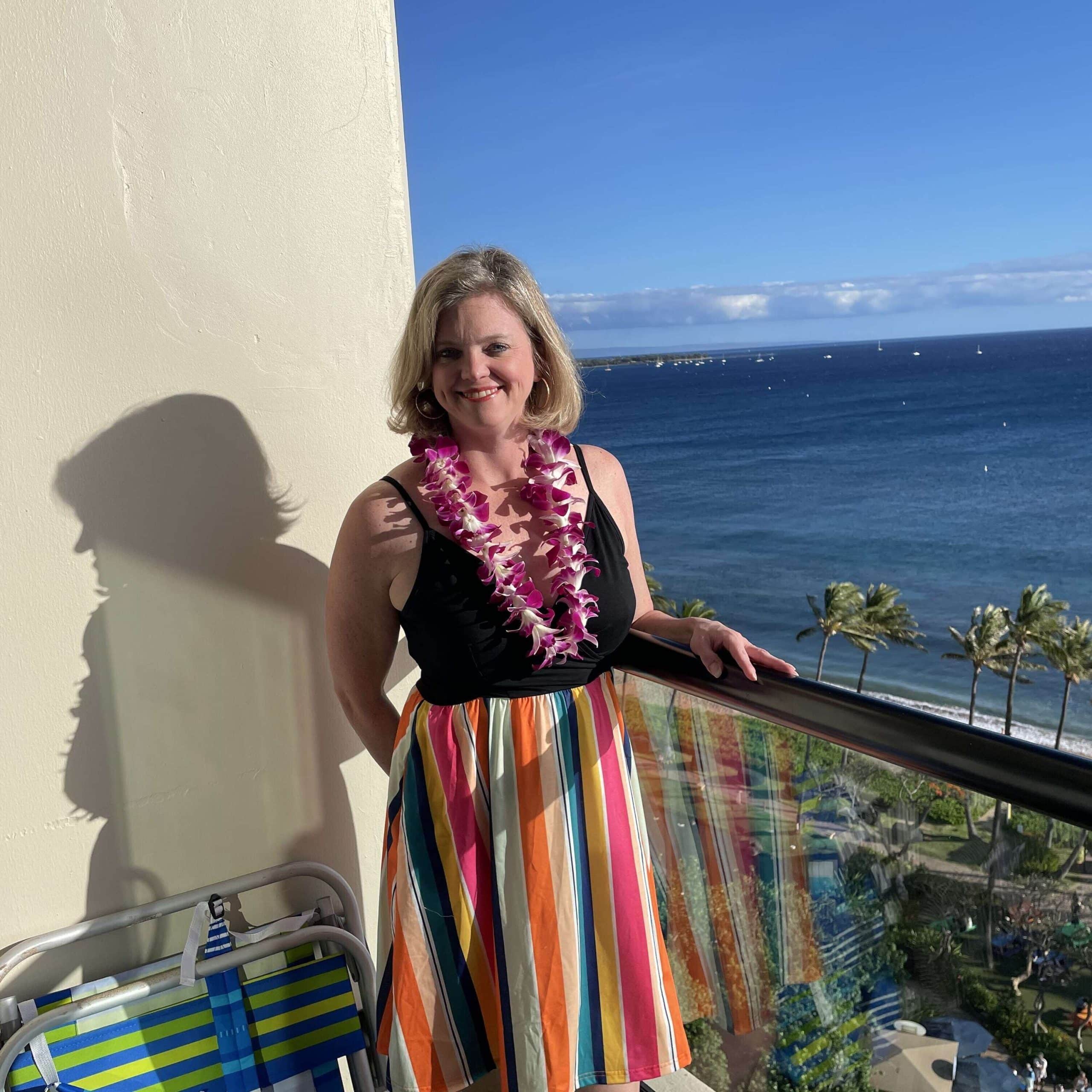 A woman in a colorful dress standing on a balcony overlooking the ocean.