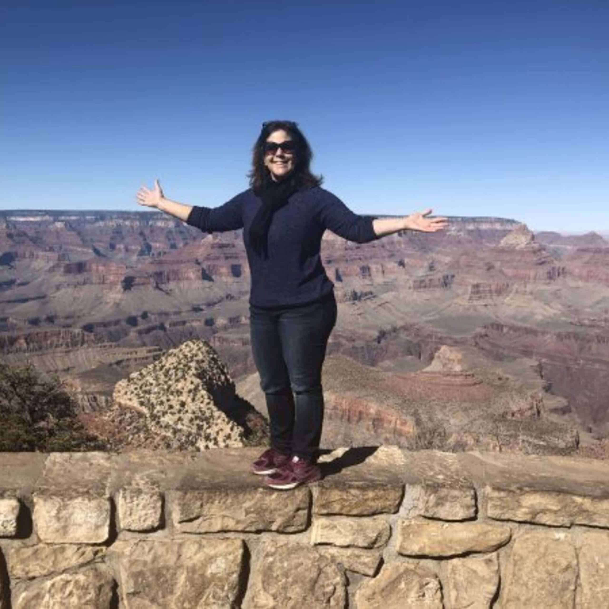 A woman standing in front of the grand canyon with her arms outstretched.