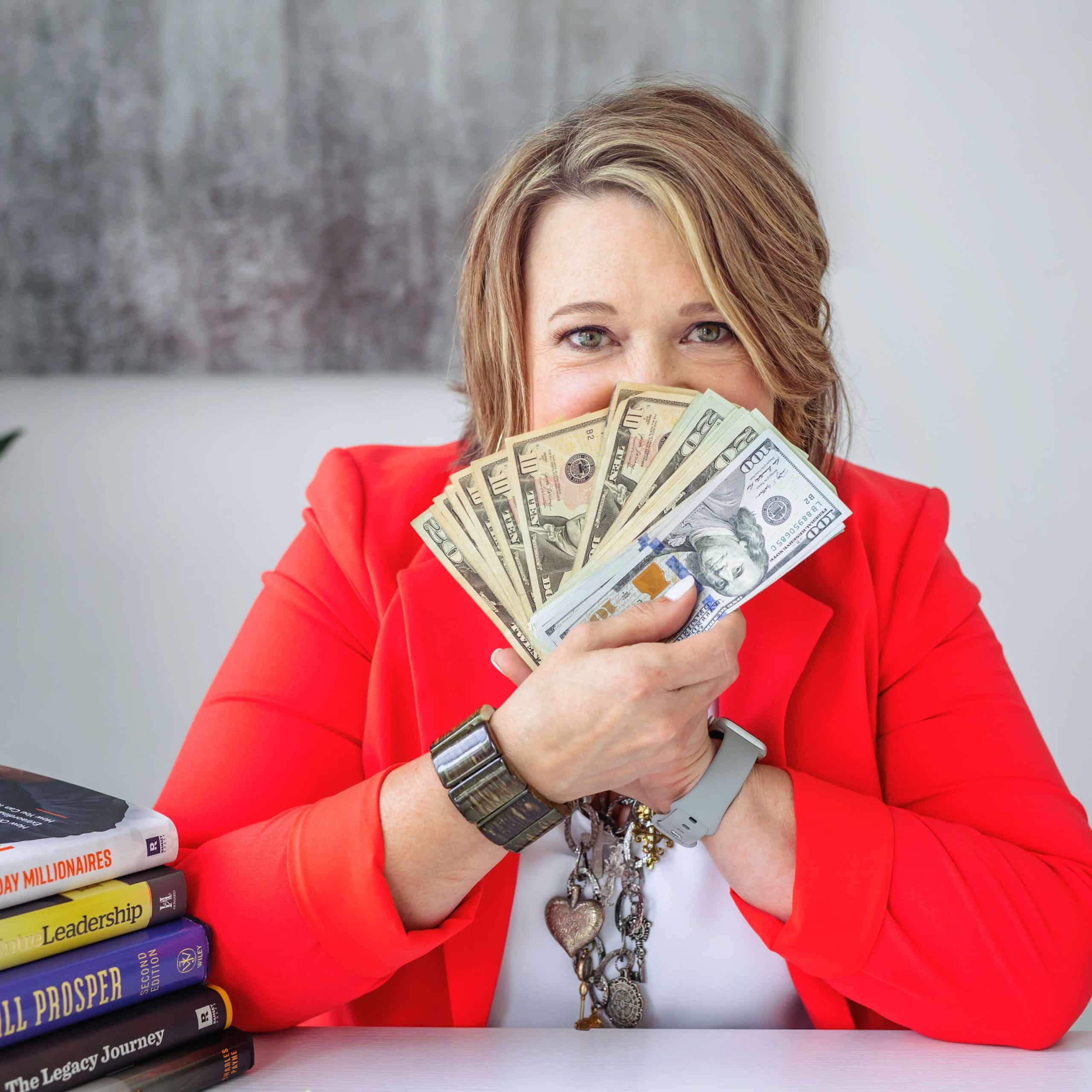 A woman with a red jacket holding money in front of a desk.