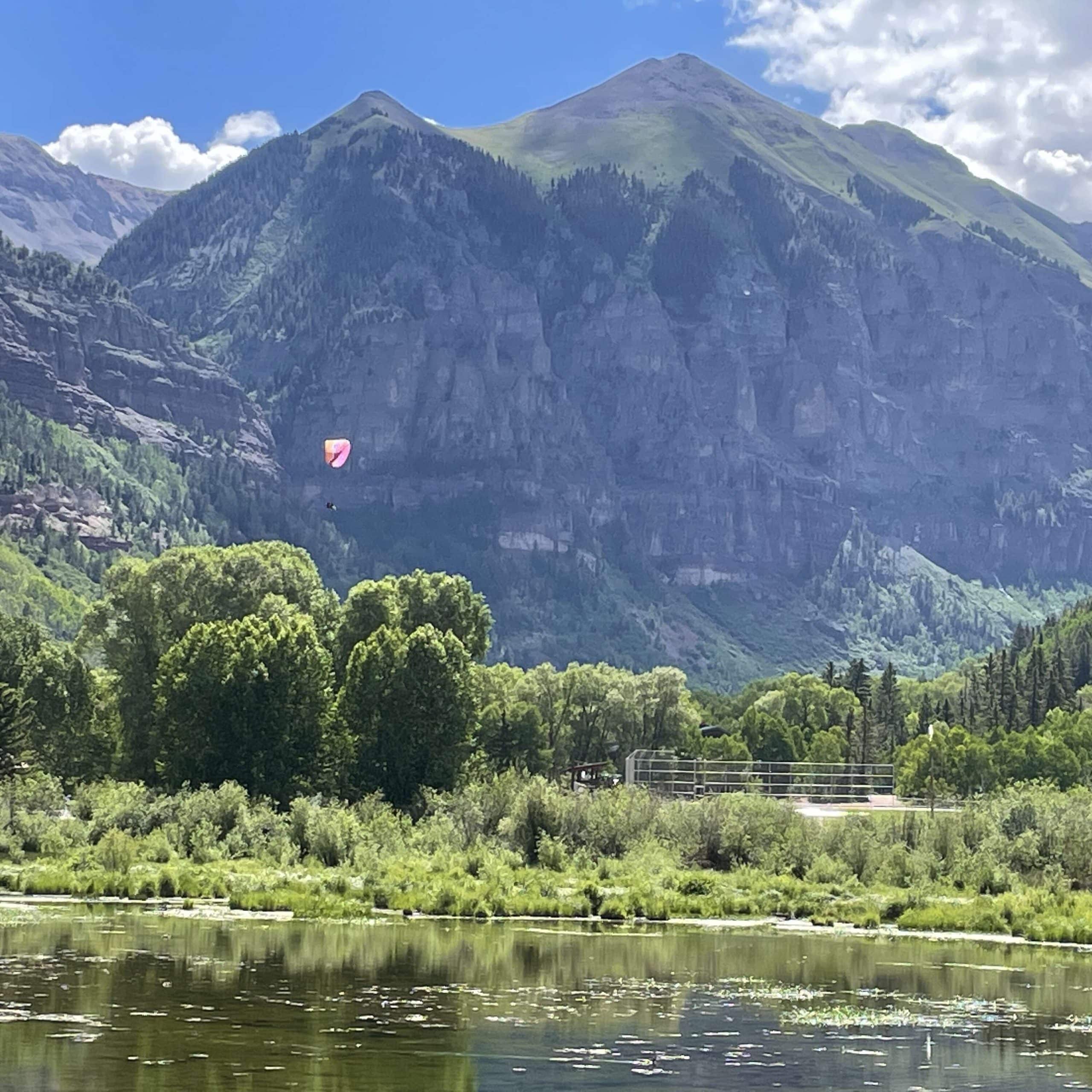 A hot air balloon flies over a river with mountains in the background.