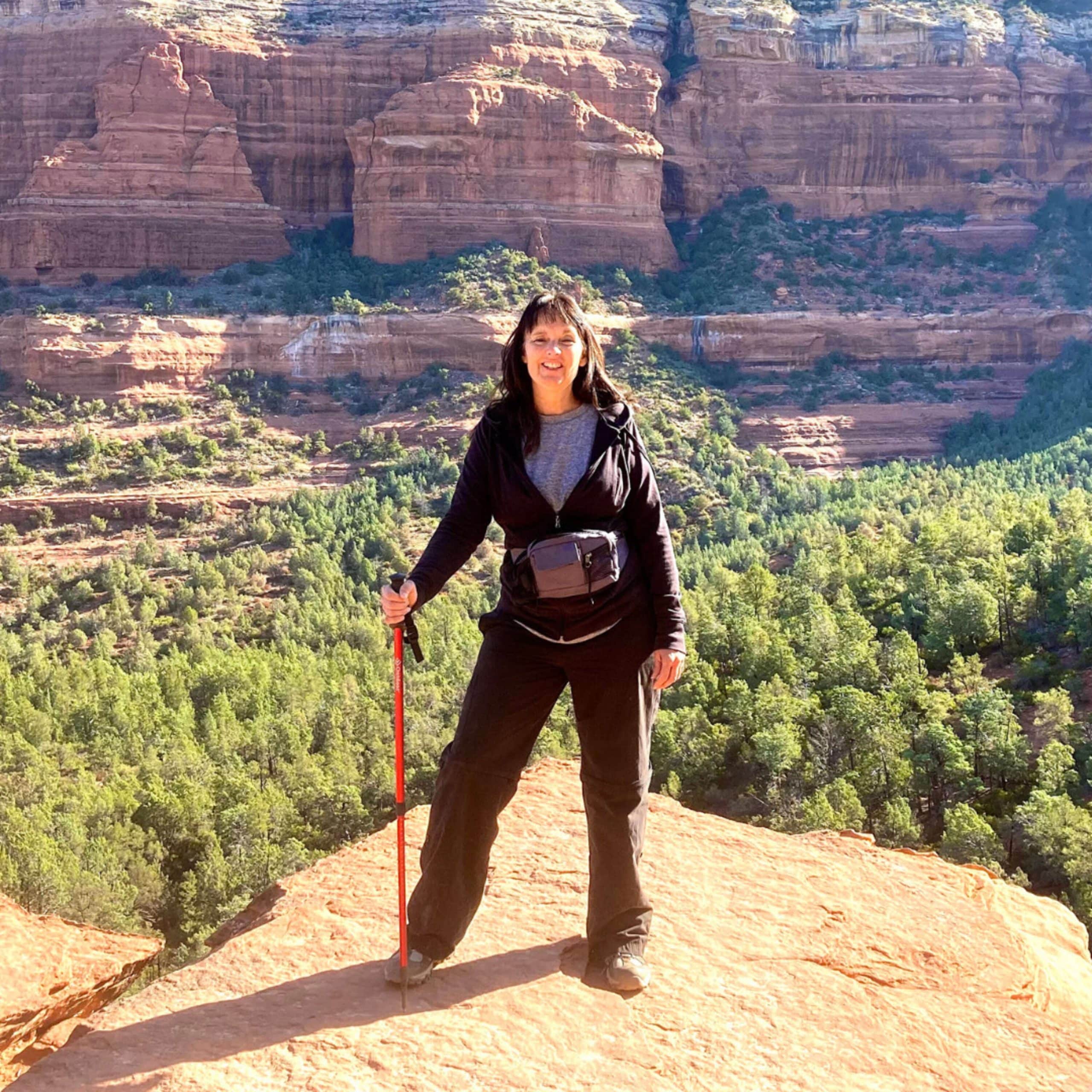 A woman standing on top of a cliff with hiking poles.