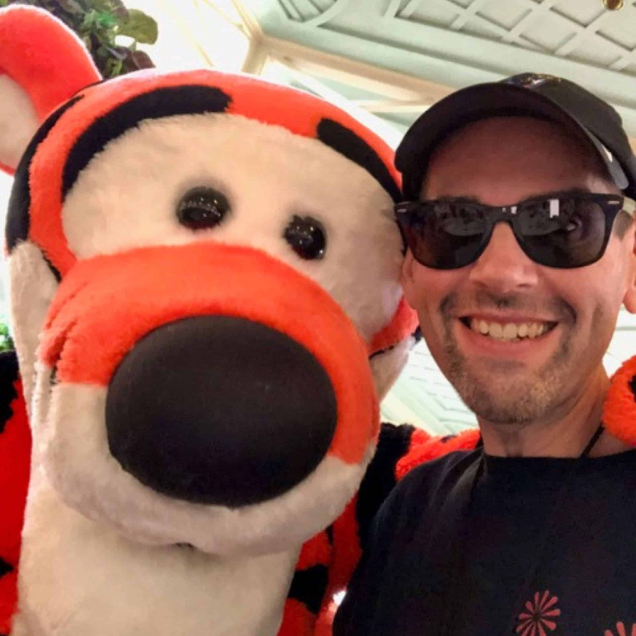 A man in sunglasses is posing with a tiger mascot.