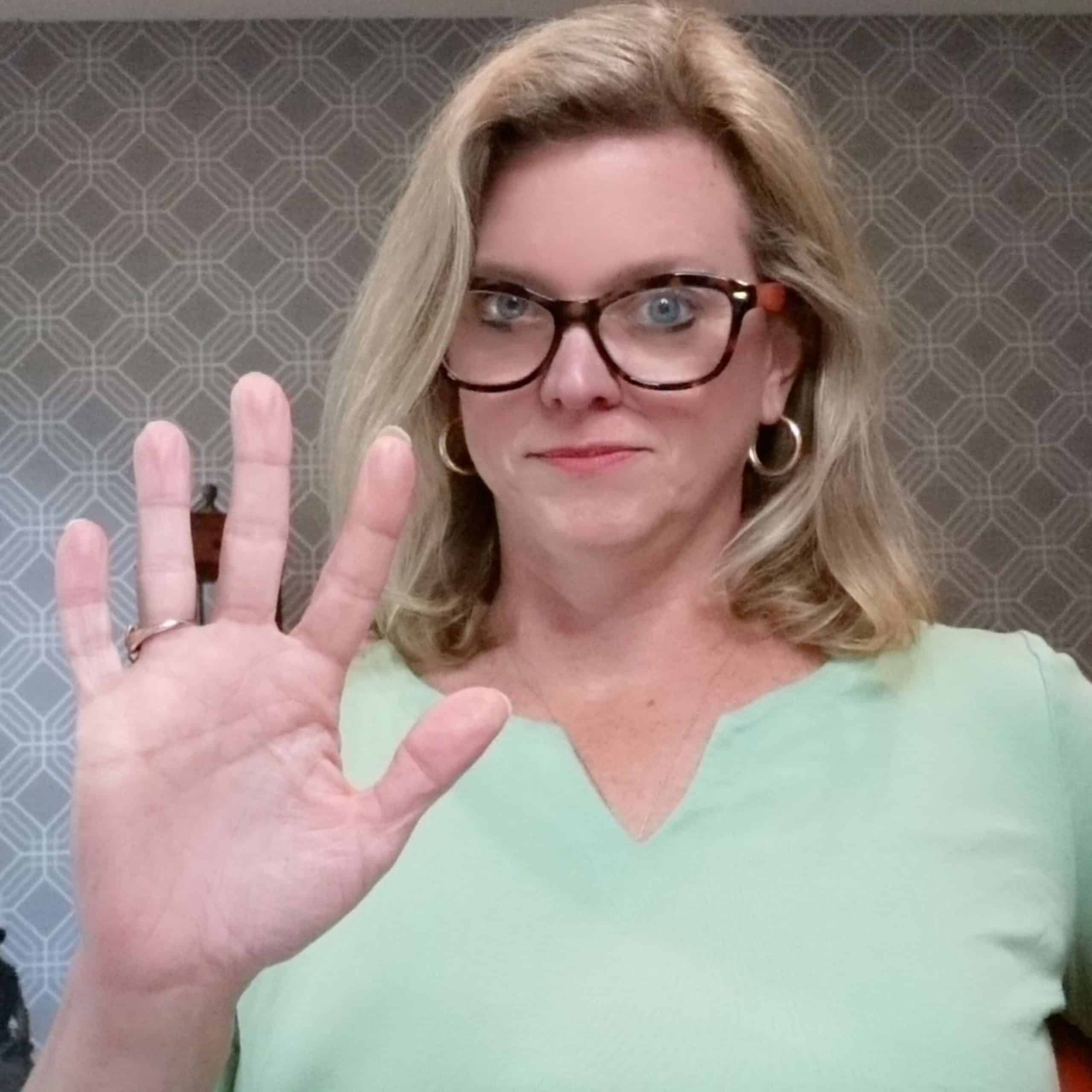 A woman wearing glasses is showing her hand in the air.