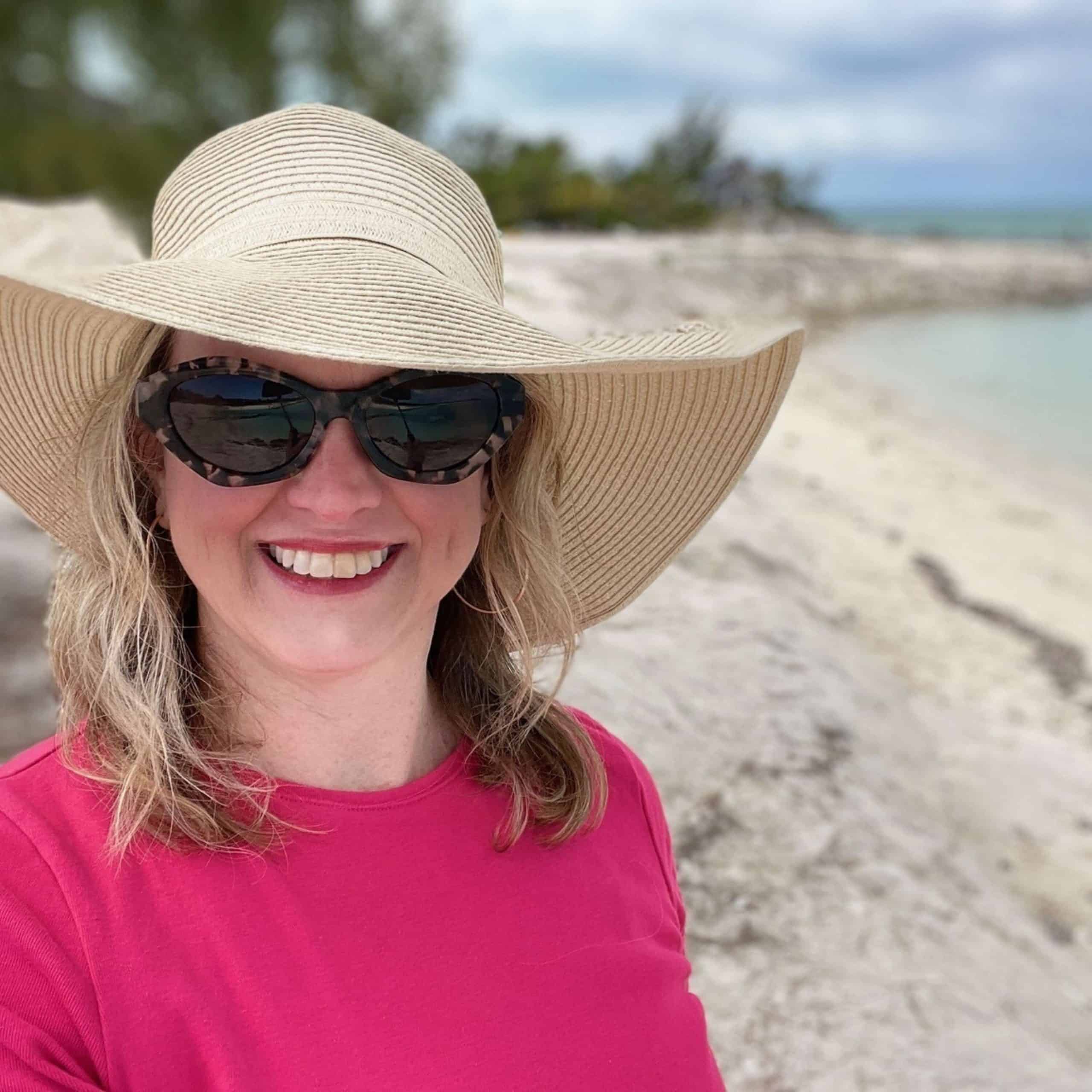 A woman wearing a hat and pink shirt on a beach.