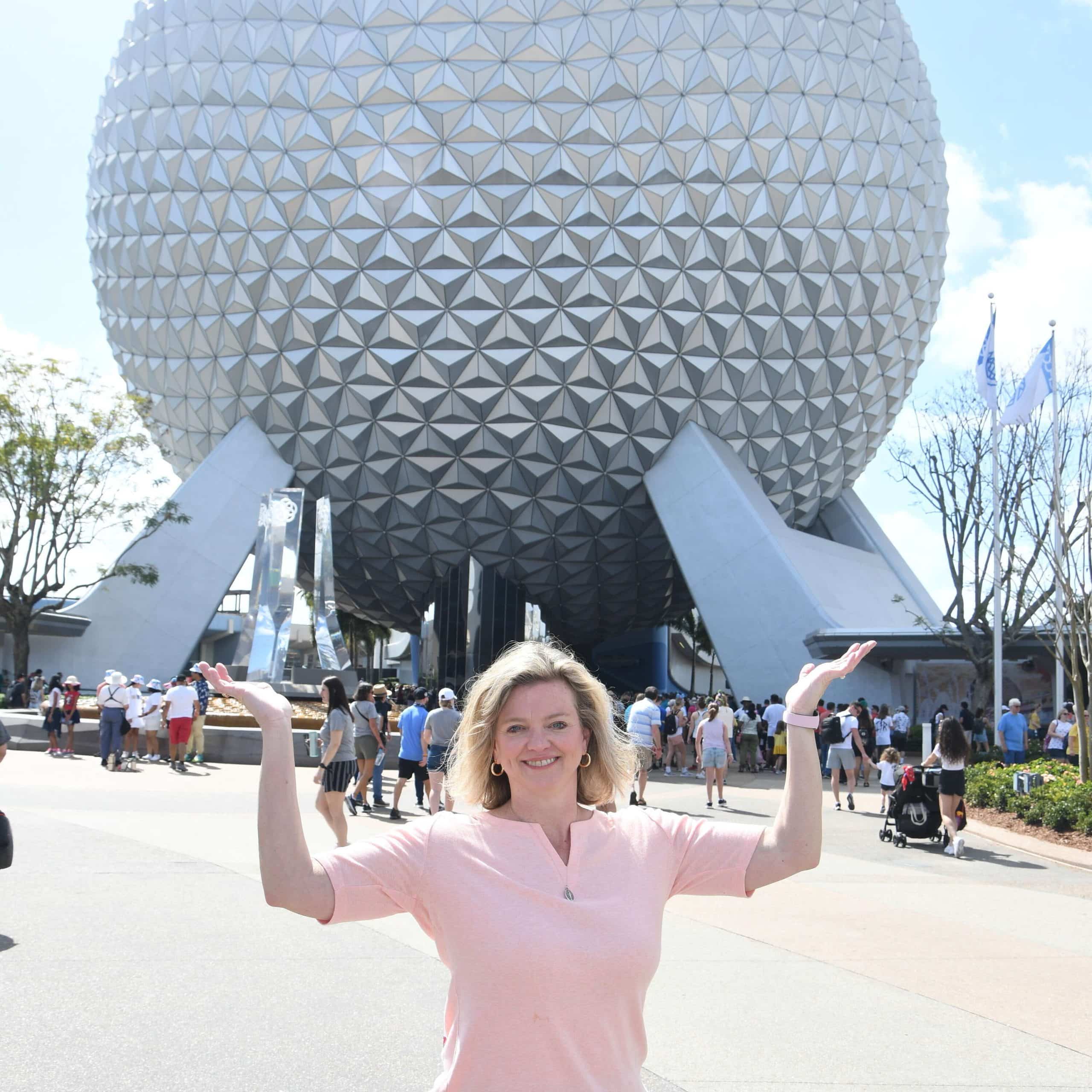 A woman standing in front of the epcot spaceship.