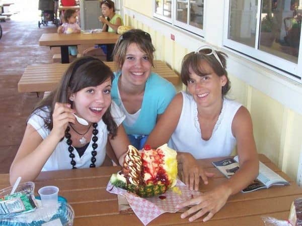 Three women sitting at a table with a cake in front of them.