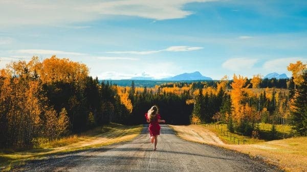 A woman is walking down a dirt road in the fall in Canada.