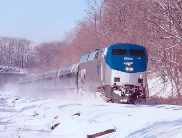 A train traveling down a snowy track with trees in the background.