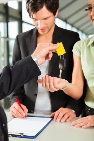 A woman from southwest car rentals handing a car key to a man in a suit.