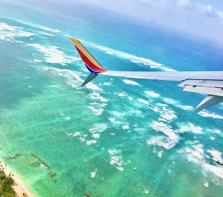 An airplane wing flying over a beach and ocean.