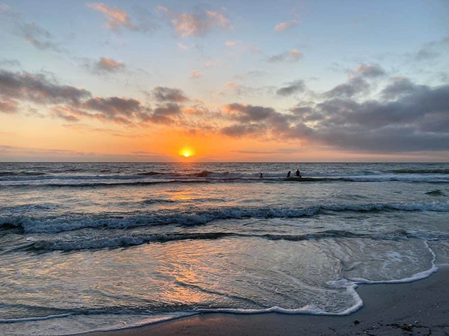 The sunset colors illuminate a beach with people enjoying the water at Tradewinds Island Grand Resort.