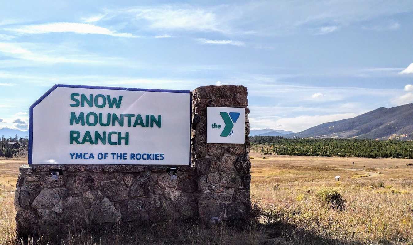 A sign for snow mountain ranch in the middle of a field.