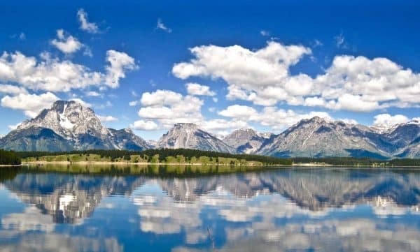 The grand teton mountain range is reflected in a lake.