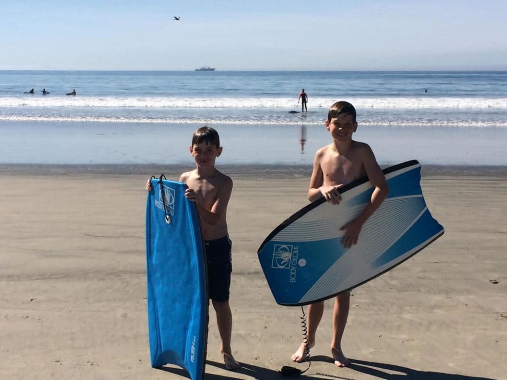 Two boys enjoying things to do in San Diego while standing on the beach holding surfboards.