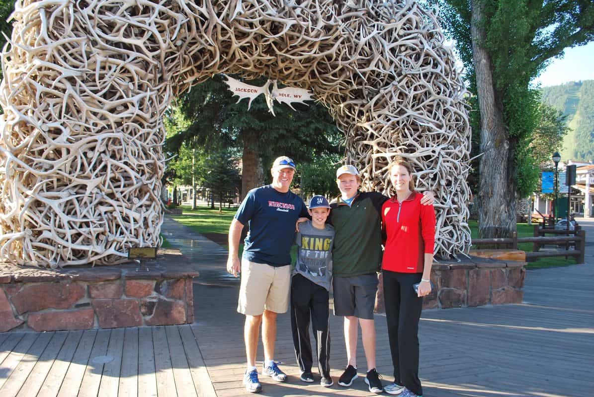 Three people posing in front of an arch made of moose antlers.