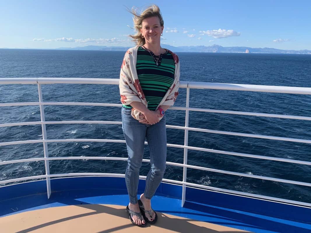 A woman wearing Oofos standing on the deck of a cruise ship.