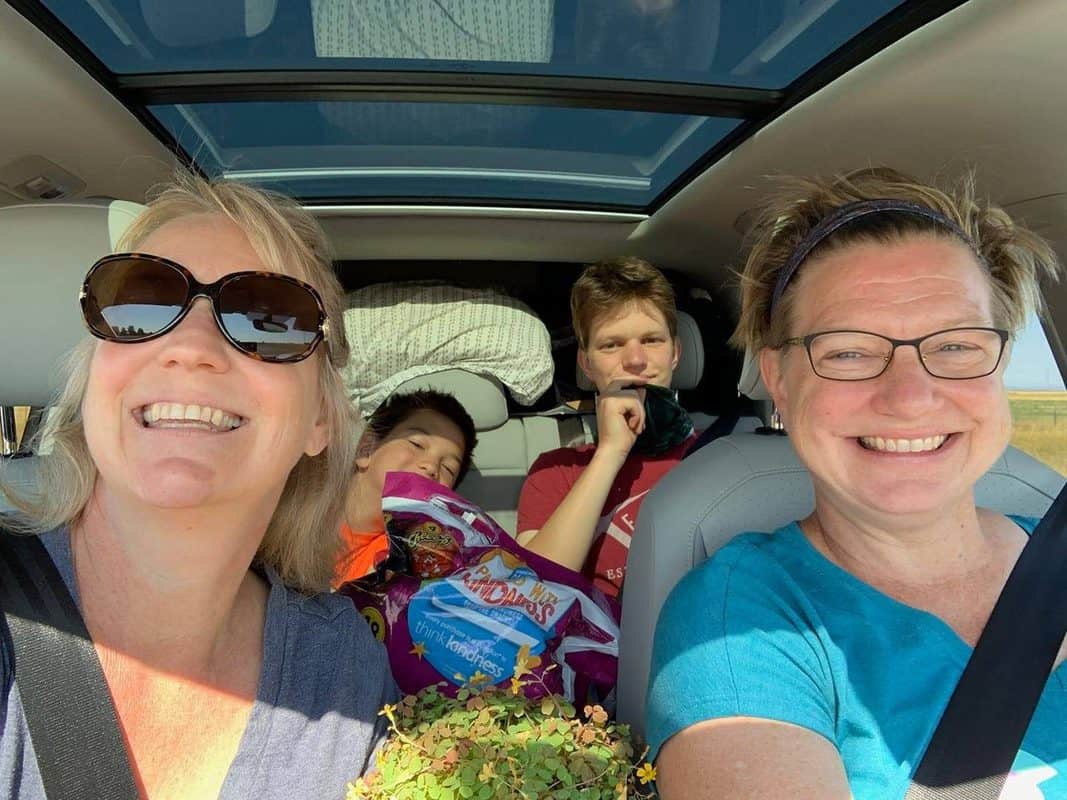 A family smiles in the back seat of a car.