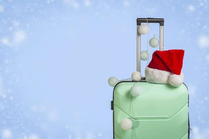 The perfect travel gift: a stylish green suitcase adorned with a festive Santa hat.