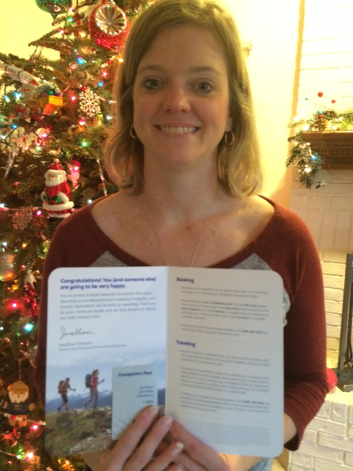 A woman holding up a brochure in front of a christmas tree.