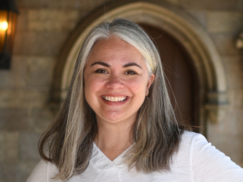 A woman with gray hair smiling in front of an archway.