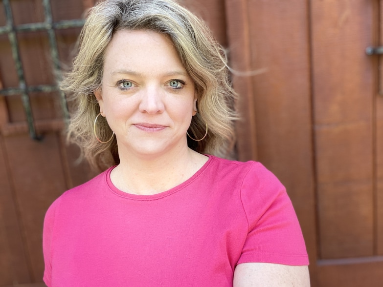 A woman in a pink shirt standing in front of a wooden door.