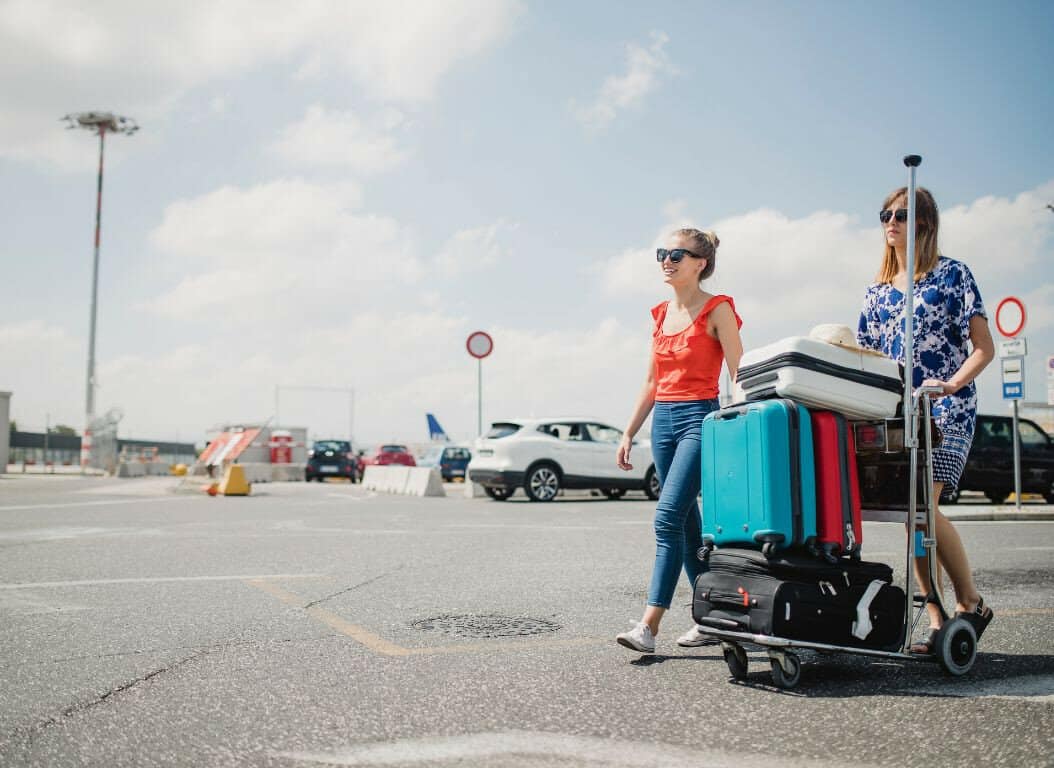 Two women walking with luggage in an airport parking lot.