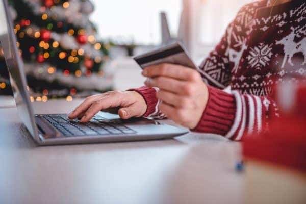 A person using a laptop with a credit card in front of a christmas tree.