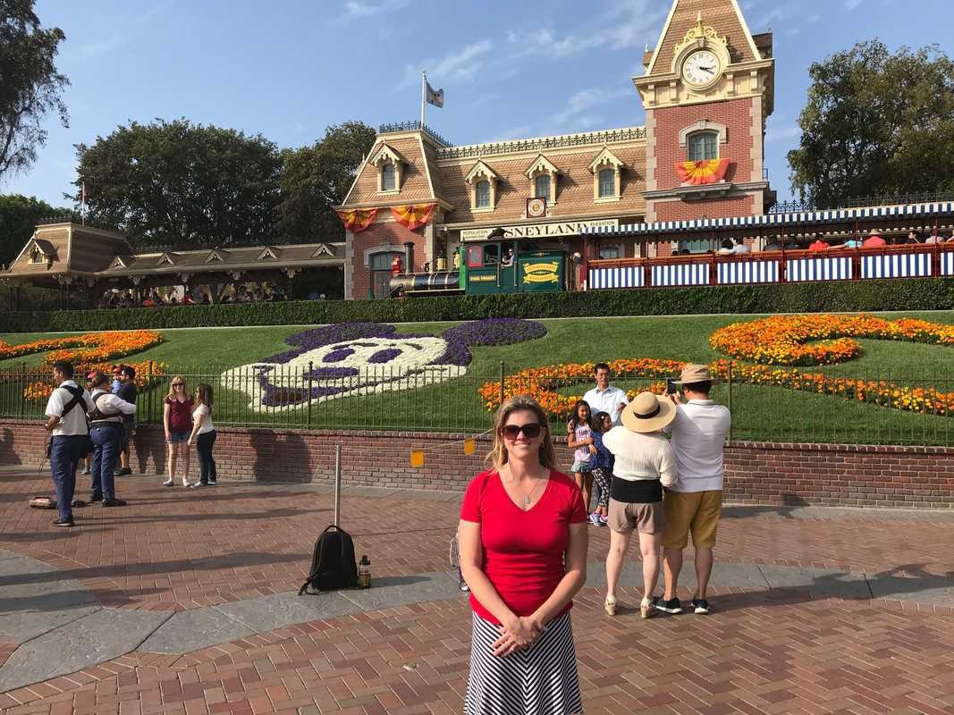 A woman standing in front of a flower garden at Disneyland during Halloween.