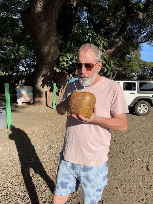 A man drinking a coconut in front of a jeep.