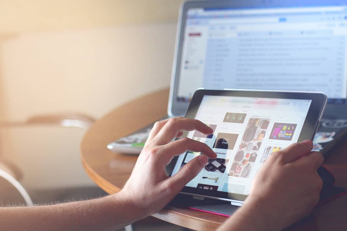 person tapping on tablet with laptop computer in background