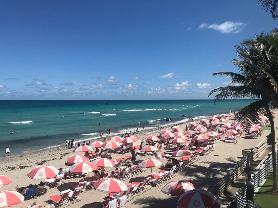 A beach with red and white umbrellas and palm trees.