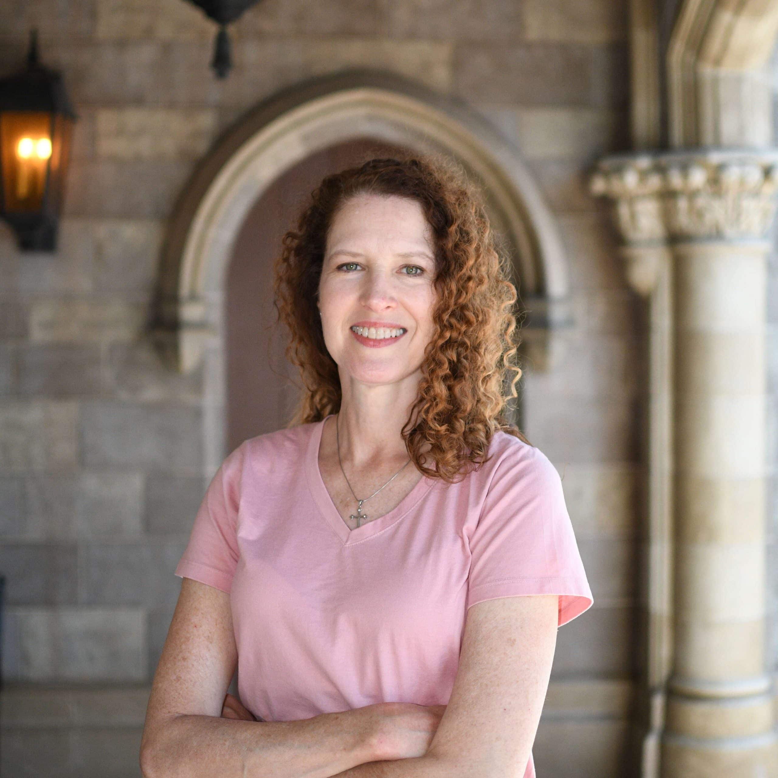 A woman in a pink shirt standing in front of an archway.