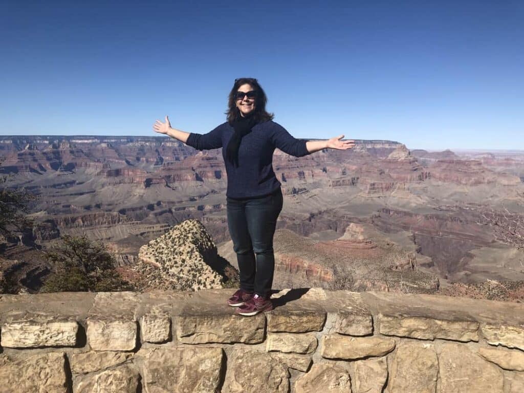 A woman on the south rim of the grand canyon, arms outstretched.