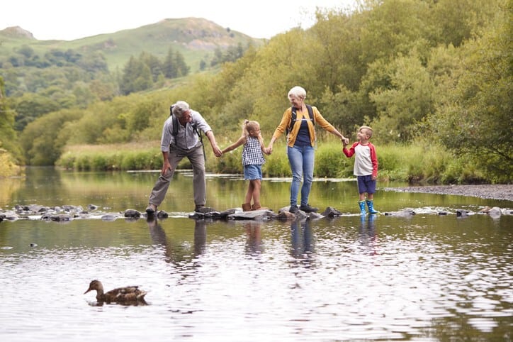 A family is walking on a bridge over a river with ducks in the background.