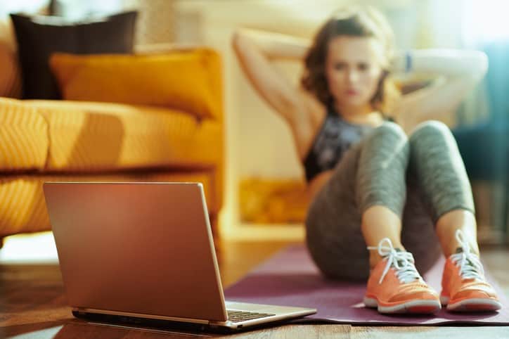 A woman is sitting on a yoga mat while using a laptop.