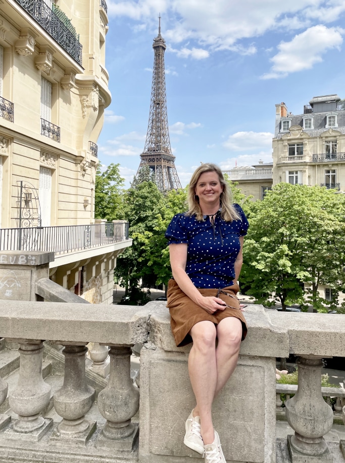 A woman sitting on a railing in front of the eiffel tower.