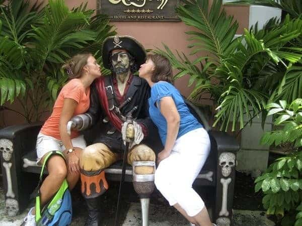 Two women enjoy the things to do in Nassau, sitting on a bench next to a statue of a pirate at Graycliff in Nassau Bahamas