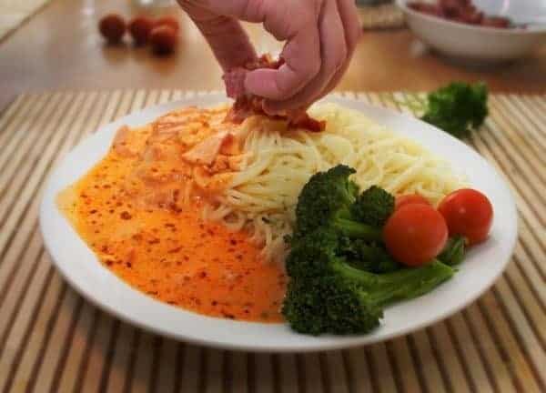 A person putting sauce on a plate of pasta.