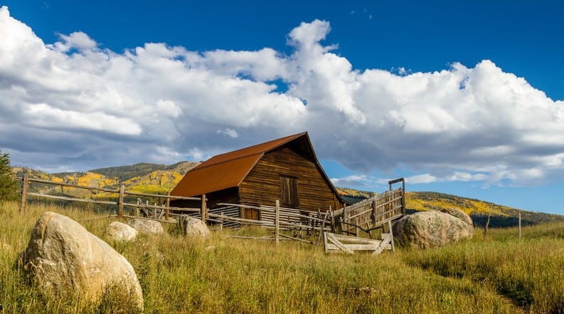 An old barn in the middle of a grassy field.