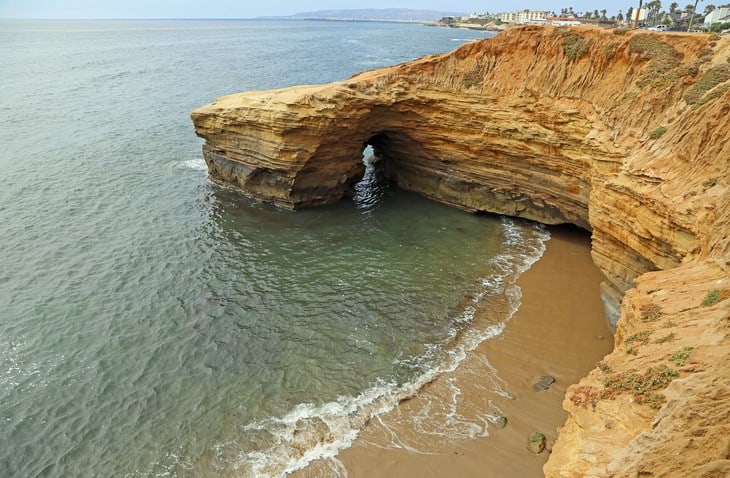 A cliff with a hole in it near the ocean.