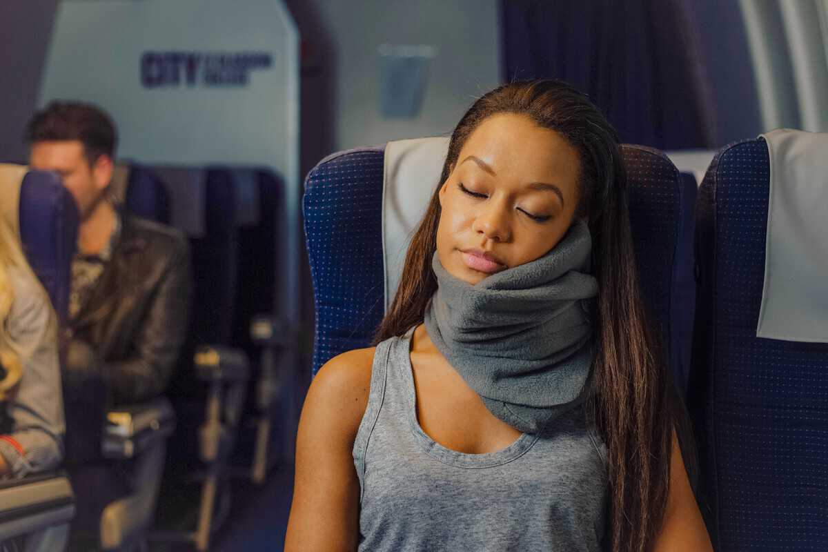 A woman sleeping on an airplane with a neck pillow.