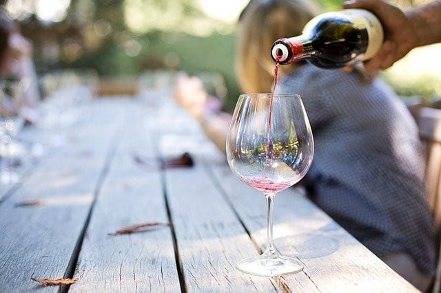 A man pouring wine into a glass on a wooden table.