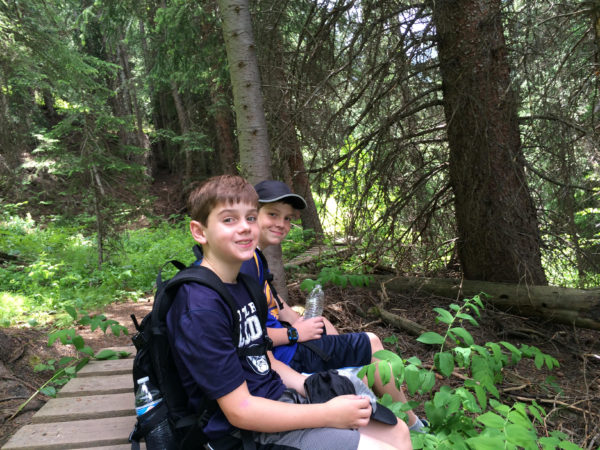 Two boys hiking on a wooden bridge in the woods, on their journey from Crested Butte to Aspen.